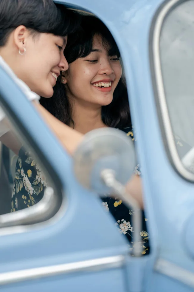 A joyful young couple laughing together inside a vintage blue car, enjoying a happy moment after their car is recovered safely in dubai
